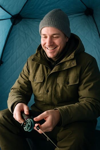 Guest angler testing an ice rod near a drilled hole at dusk
